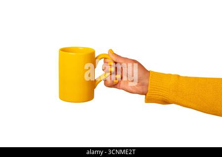 Gros plan d'une main en pull jaune tenant une tasse jaune assortie sur fond blanc, parfait pour la marque, la publicité et les concepts de style de vie. Banque D'Images