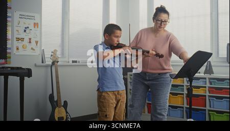 Garçon talentueux jouant du violon pendant la leçon de musique à l'école primaire, répétant avant la performance musicale. Enseignant soutenant et enseignant futur musicien. Éducation musicale, cours de pratique du violon. Banque D'Images