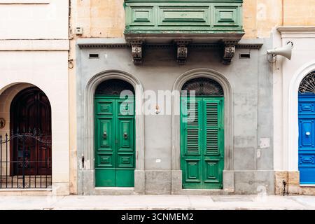 Façade maltaise traditionnelle avec deux portes vertes et balcon en bois assorti dans la ville historique de Mosta, avec des cadres voûtés et d architectural Banque D'Images