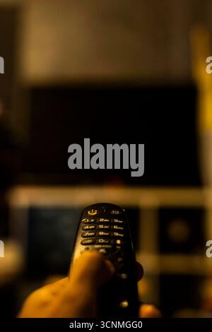 Utilisez la télécommande du téléviseur dans Dark Room, une scène authentique conçue pour le marketing électronique, des visuels confortables et des contenus de loisirs ou de style de vie moderne. Banque D'Images