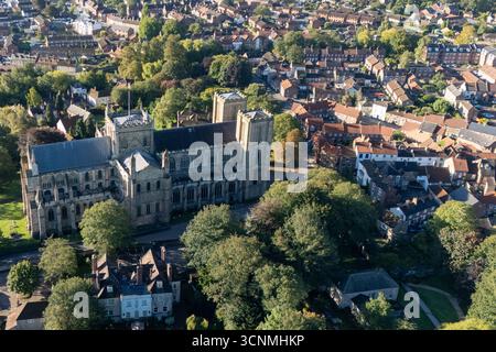 Photographie aérienne de la cathédrale de Ripon à Ripon, Yorkshire du Nord, Royaume-Uni, capturée par temps clair de fin d'été avec un ciel bleu vif et un soleil chaud mettant en valeur l'architecture gothique saisissante de la cathédrale. L'image montre l'élégant front ouest anglais ancien avec ses tours jumelles, ses pierres complexes et ses fenêtres cintrées, entouré par les rues historiques de la ville, les bâtiments voisins, les toits et les parcelles d'espaces verts, y compris les parcs et les espaces ouverts. Cette vue aérienne d'un drone capture la position centrale de la cathédrale dans la ville médiévale compacte, soulignant son rôle en tant que monument historique clé Banque D'Images