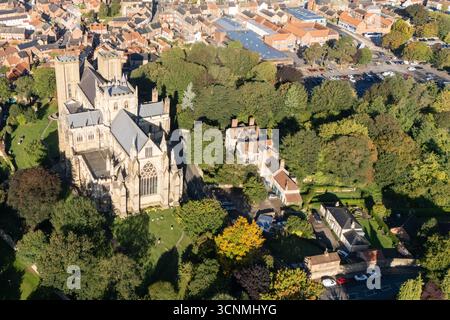 Photographie aérienne de la cathédrale de Ripon à Ripon, Yorkshire du Nord, Royaume-Uni, capturée par temps clair de fin d'été avec un ciel bleu vif et un soleil chaud mettant en valeur l'architecture gothique saisissante de la cathédrale. L'image montre l'élégant front ouest anglais ancien avec ses tours jumelles, ses pierres complexes et ses fenêtres cintrées, entouré par les rues historiques de la ville, les bâtiments voisins, les toits et les parcelles d'espaces verts, y compris les parcs et les espaces ouverts. Cette vue aérienne d'un drone capture la position centrale de la cathédrale dans la ville médiévale compacte, soulignant son rôle en tant que monument historique clé Banque D'Images