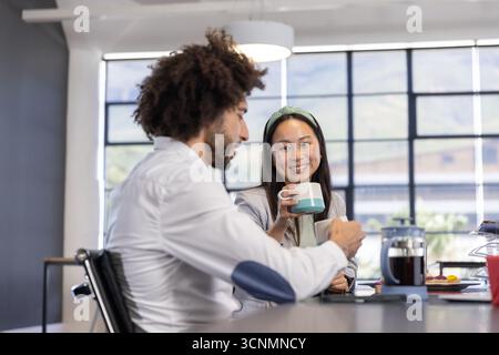Divers collègues sirotant du café dans des tasses par la presse française, discutant dans la zone de pause près de la fenêtre Banque D'Images