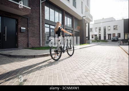 Vue arrière de la femme sportive marchant avec vélo dans la zone urbaine Banque D'Images