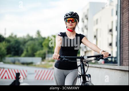 Femme en casque et lunettes marchant à l'extérieur avec vélo Banque D'Images