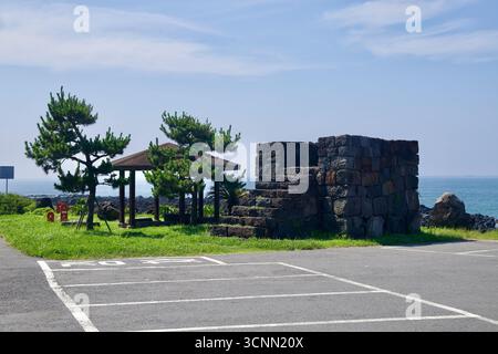 Une plate-forme carrée en pierre et un pavillon d'ombrage se dressent à côté de pins en forme de vent sur la rive basaltique près de Sinheung-ri, surplombant la mer ouverte. Banque D'Images