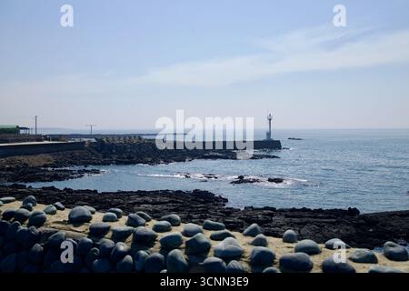 Une balise blanche du port se dresse au bout d'un brise-lames au-delà d'un mur bas coiffé de pierres arrondies, surplombant les récifs de lave noirs et les petits surf sur J. Banque D'Images
