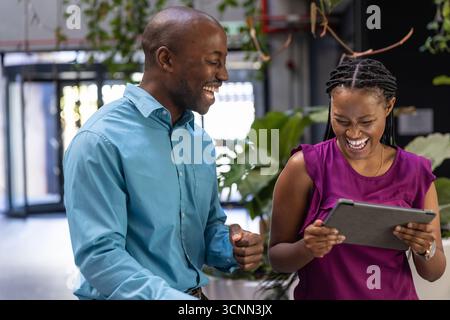 Collègues afro-américains en tenue d'affaires souriants, discutant de tablette dans le hall du bureau Banque D'Images