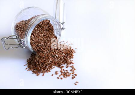 Graines de lin versées dans un bocal en verre isolé sur un fond blanc. Les graines de lin sont riches en fibres, en acides gras oméga-3 et en lignanes. Banque D'Images