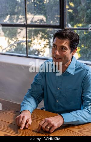 Homme portant une chemise bleu clair pointant vers la table par une grande fenêtre, espace de copie Banque D'Images