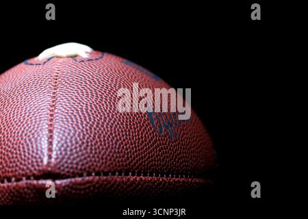 Un gros plan d'un football américain révèle une texture de cuir détaillée et des coutures précises, photographiées en studio sur fond noir, highli Banque D'Images