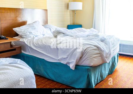 Lit non fait grondé dans une chambre d'hôtel lumineuse et ensoleillée, draps, oreillers et couette le matin, détendu et habité, concept de voyage, dormir Banque D'Images