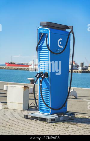 BURGAS, Bulgarie - 20 septembre 2025 : borne de recharge de véhicule électrique de couleur bleu vif, située au bord de l'eau avec des navires en arrière-plan, moderne Banque D'Images