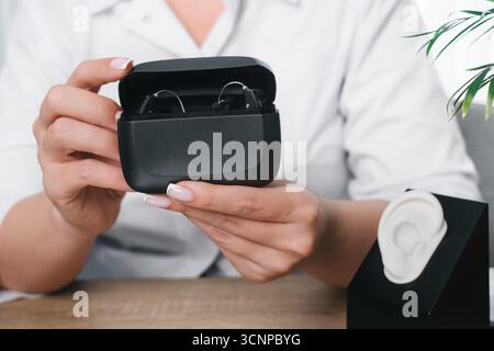 Mains de médecins tenant un étui de charge ouvert avec deux aides auditives numériques. Technologie d'assistance moderne pour la santé auditive et l'utilisation quotidienne Banque D'Images