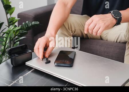 Aides auditives numériques modernes, smartphone et étui de chargement sur une table de bureau élégante, avec une personne préparant les appareils pour le travail. Environnement professionnel Banque D'Images