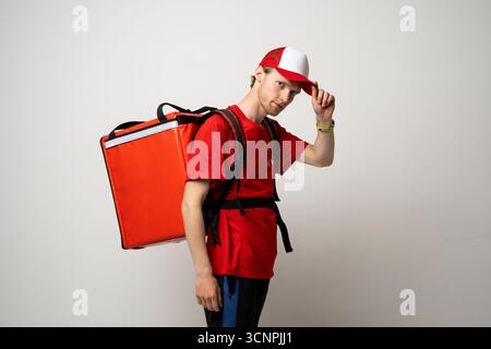 Coursier en uniforme rouge et casquette transportant un sac à dos isolé regardant la caméra Banque D'Images