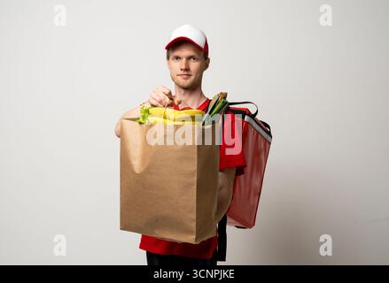 Coursier en uniforme rouge tenant le sac d'épicerie plein de fruits et légumes Banque D'Images