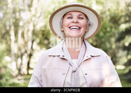 Femme âgée souriante portant un chapeau et des vêtements décontractés légers, portrait rapproché joyeux à l'extérieur, style de vie positif d'âge, bonheur, beauté naturelle, conf Banque D'Images