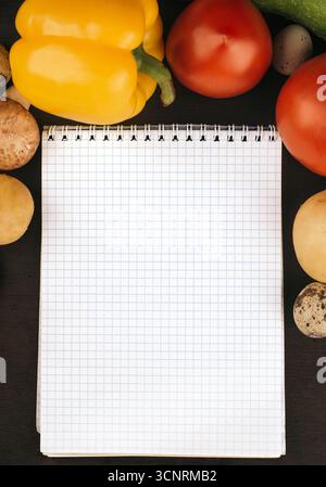 Cahier vierge entouré de divers légumes frais et œufs de caille sur un fond sombre Banque D'Images