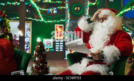 Le Père Noël hoche la tête, en désaccord avec les lettres reçues des enfants. Personne en costume de Noël lit des listes de souhaits écrites par des enfants demandant des cadeaux coûteux, faisant trembler la tête désapprouvant, caméra A. Banque D'Images