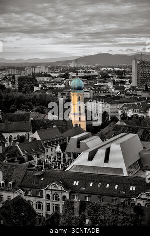 Une vue spectaculaire en hauteur de Graz mettant en évidence la tour aux couleurs vives de la Mariahilferkirche sur un fond de ville désaturé Banque D'Images