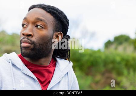 Homme afro-américain adulte regardant à gauche dans le parc avec anneau de nez et boucle d'oreille, espace de copie Banque D'Images