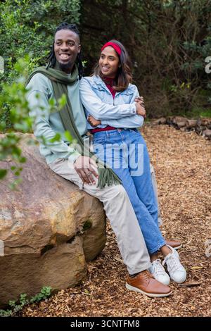 Couple diversifié se penchant les uns dans les autres sur le rocher dans la forêt de défrichement portant un bandeau rouge foulard vert Banque D'Images