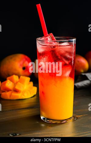 Mangue glacée Hibiscus Tea superposé dans un grand verre avec de la paille : fruit et tisane servis sur glace dans un gobelet avec de la paille avec des mangues fraîches Banque D'Images