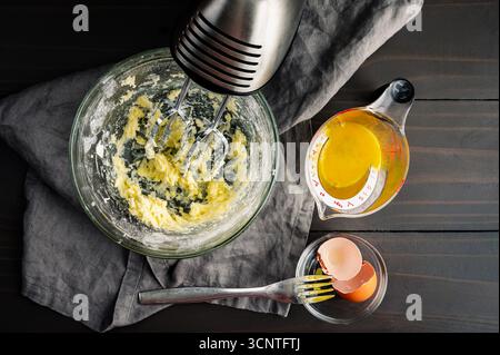 Beurre à la crème et sucre en poudre dans un bol à mélanger en verre : beurre fouetté et sucre de confiserie avec un batteur à main, œuf battu et fourchette Banque D'Images