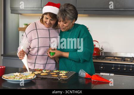 Mère et fille diversifiées décorant des biscuits de vacances sur le comptoir en pierre sombre avec des sacs à passepoil Banque D'Images