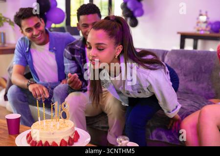 Divers amis adolescents célébrant autour du gâteau sur la table basse à la maison sous des ballons Banque D'Images