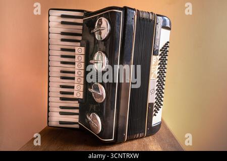 Vieil accordéon noir avec des touches de piano et des boutons de basse placés sur une surface en bois sur fond de mur chaud Banque D'Images