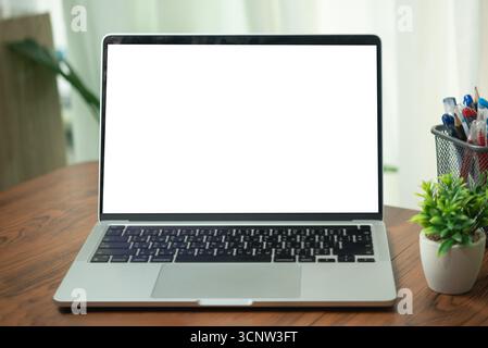 Ordinateur portable ouvert avec un écran blanc vierge sur un bureau en bois avec plante en pot et porte-stylo, représentant un espace de travail propre et organisé. Banque D'Images