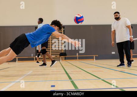 Divers coéquipiers masculins et entraîneur regardant le joueur plonger pour le volley à côté des bars de gymnastique, espace de copie Banque D'Images