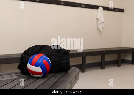Sac de sport noir et ballon de volley rouge blanc et bleu reposant sur le banc dans le vestiaire Banque D'Images