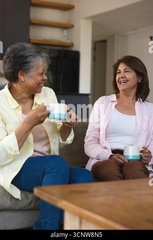 Diverses amies féminines discutant sur le canapé dans le salon tout en sirotant des tasses en céramique sarcelle et blanc Banque D'Images