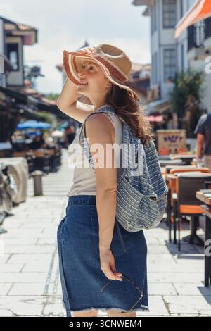 Une femme touriste profite d'une journée ensoleillée à pied dans les charmantes rues historiques d'Antalya, en Turquie, portant un chapeau de soleil et un sac à dos, capturant le Banque D'Images