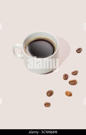 Une tasse à café en céramique blanche remplie de café noir se trouve sur un fond clair, accompagnée de grains de café torréfiés dispersés, évoquant une sensation de chaleur Banque D'Images