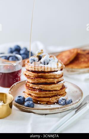 Une délicieuse pile de crêpes maison garnies de bleuets frais et d'un filet de sirop d'érable. Le sucre en poudre est légèrement saupoudré sur le dessus, créant un Banque D'Images