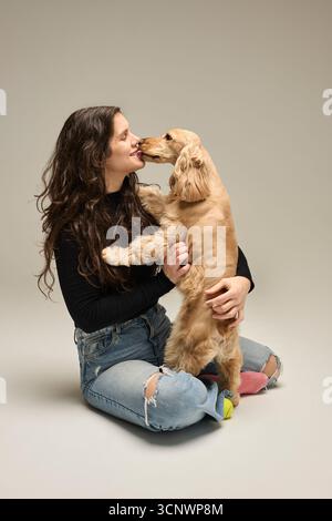 Une femme est assise sur le sol, embrassant avec amour son chiot spaniel cocker ludique. Le chiot, plein d'énergie et d'affection, se ronge ludique le visage, sho Banque D'Images