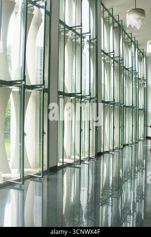 Fenêtres en verre modernes au design abstrait - Un couloir avec une longue rangée de fenêtres en verre modernes présentant un design abstrait courbe répété, réfléchissant Banque D'Images