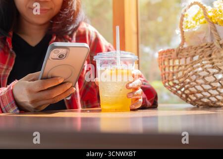 Femme asiatique adulte au café buvant du thé glacé et utilisant le téléphone portable dans le café. Mise au point sélective. Banque D'Images