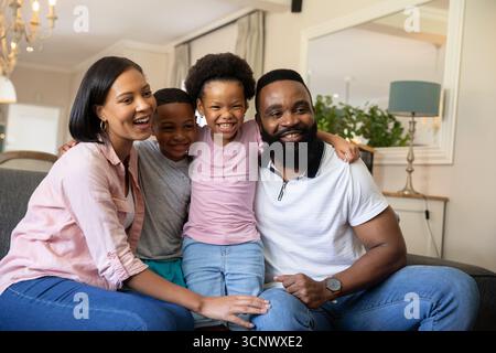 Famille diversifiée assis sur un canapé gris dans le salon avec miroir mural, lampe d'abat-jour bleu et lustre Banque D'Images