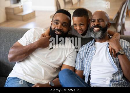 Famille afro-américaine assise sur un canapé gris foncé dans un salon lumineux près de chaises empilées Banque D'Images