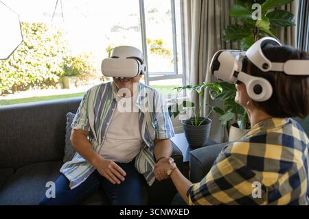 Couple senior portant des casques vr tenant les mains assis sur le canapé dans le salon Banque D'Images