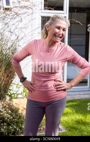 Femme senior debout avec les mains sur les hanches dans le jardin d'arrière-cour portant une tenue athlétique Banque D'Images