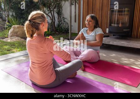 Diverses amies féminines pressant les paumes ensemble sur des tapis de yoga dans le salon près de la cheminée Banque D'Images