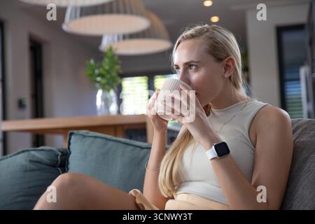 Femme assise sur le canapé dans le salon tenant la tasse en céramique côtelée aux lèvres, espace de copie Banque D'Images