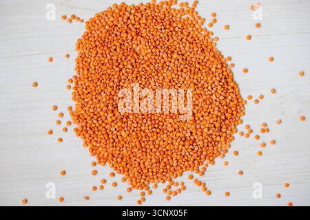 Lentilles rouges crues dispersées sur une table en bois. Les lentilles rouges sont également connues sous le nom de masoor dal, lentilles orange et lentilles roses. Banque D'Images
