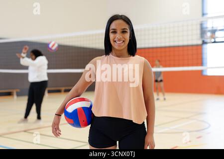 Diverses coéquipières féminines pratiquant le volleyball sur un terrain de gymnase, balle rouge blanc bleu et filet Banque D'Images